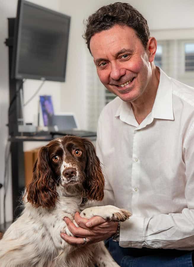 Sean Leane WUF design A headshot of a smiling man wearing a plaid shirt with a dark background.